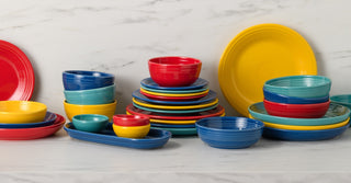 Stacks of colorful ceramic plates and bowls, including shades of orange, pink, red, blue, green, yellow, and white, arranged in an orderly, eye-catching display.