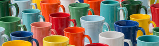 A group of colorful ceramic mugs, including red, blue, yellow, green, orange, pink, and white, are arranged closely together in rows, creating a vibrant and cheerful pattern.