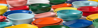 An assortment of colorful ceramic bowls and plates, including green, red, blue, yellow, orange, pink, teal, and white pieces, arranged in a scattered pattern on a flat surface.