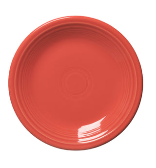 A round, empty, coral-colored ceramic plate with concentric raised rings near the center, shown on a white background.