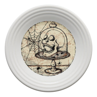 A white plate features an illustration of a skull on a pedestal under a glass dome, surrounded by spiders and a cobweb in the background.