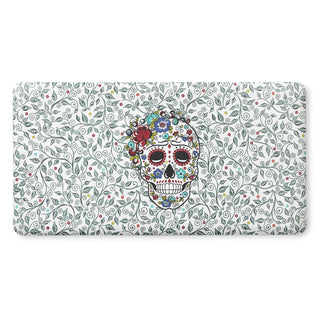 A colorful sugar skull decorated with flowers is centered on a white background with a pattern of swirling green vines and small red, yellow, and blue flowers.