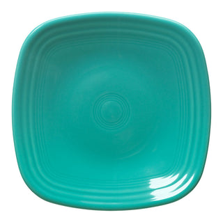 A turquoise, square ceramic plate with rounded edges and a glossy finish, featuring concentric circular patterns in the center.