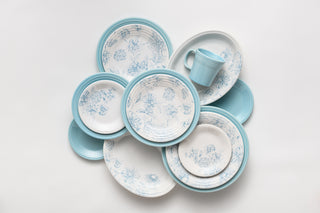 A collection of blue and white floral-patterned plates arranged in a circular pattern with a light blue mug placed on top, all set against a white background.