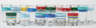 A collection of clear drinking glasses with colorful bands in green, yellow, blue, red, and turquoise, arranged in rows on a white background.