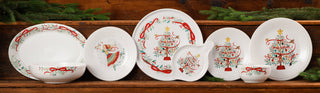 A festive table is set with holiday-themed plates, candles, bread rolls, a glass of red wine, and evergreen branches, with a decorated Christmas tree glowing in the background.