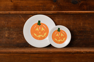 Two white plates with smiling jack-o’-lantern pumpkin designs sit on a wooden surface, one plate larger than the other.