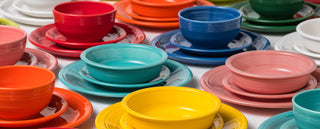 Colorful ceramic bowls, plates, and cups are arranged in matching sets on a white surface. The sets include vibrant reds, blues, yellows, oranges, greens, and pinks.