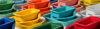 Stacks of colorful rectangular plastic containers in various colors, including yellow, red, blue, teal, pink, white, and gray, are arranged closely together on a white surface.