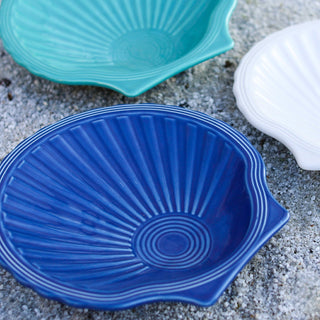 Three Fiesta Retired Shell Shaped Plates (8 1/4") in blue, teal, and white from the Coastal Collection are arranged on sand. Each plate's ridged texture radiates from the center—an ocean-inspired accent for your table.