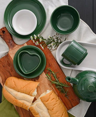 A top-down view shows green and white ceramic dishes, a green teapot, and cups on a wooden board with herbs, flowers, and torn baguette. Featured is the Fiesta 7 OZ Heart Shaped Ramekin 4 1/2 Inch by Fiesta.