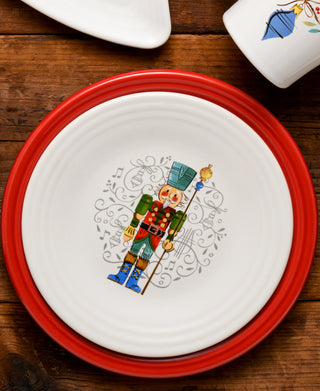 The Fiesta Nutcracker The Guardian Classic Rim 9 Inch Luncheon Plate, made in the USA, showcases a colorful nutcracker with staff amid musical notes on a white plate with red rim—perfect for festive meals.