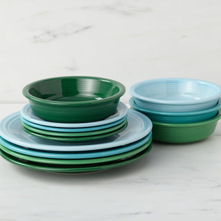 Fiesta’s Mixed Aegean Classic Rim 12-Piece Dinnerware Set, Service for 4, in green and light blue tones, sits stacked on a white marble surface, with plates and shallow bowls arranged in two tidy piles.