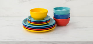 A stack of colorful plates and bowls, including yellow, red, blue, and turquoise, arranged neatly on a white marble surface against a light background.