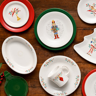 The Fiesta Retired Holly Berry Christmas Classic Rim 10 1/2 Inch Dinner Plate is displayed on a wooden table, featuring festive holly designs in red, green, and gold accents for your holiday gatherings.