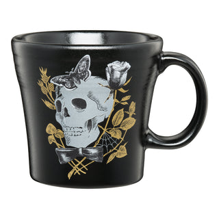 The Fiesta Retired Tapered Mug Gothic Victorian is a black ceramic mug with a skull, moth, bow tie, rose, and gold-toned botanicals. Made in the USA, it's dishwasher safe for easy cleaning.