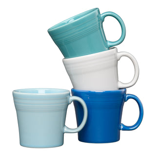 The Fiesta Mixed Coastal Blues 15 OZ Set of 4 Mixed Tapered Mug Set features blue, white, and turquoise ceramic mugs stacked unevenly against a white background. Each mug is dishwasher safe—style and convenience for your daily brew.