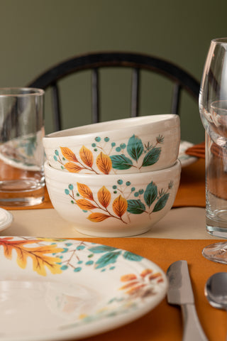 Two Fiesta Autumn Fields Bistro Coupe 5 1/2 Inch Cereal Bowls (22 oz), made in the USA and featuring autumn leaf and berry designs, are stacked on a table set for dining, with a dark wooden chair and green wall in the background.