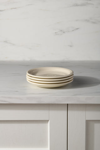 A stack of four Fiesta Linen Set of 4 Bistro Coupe 7 1/4 Inch Salad Plates sits on a light marble countertop with subtle gray veining, complemented by matching marble and white paneled cabinet doors in the background.