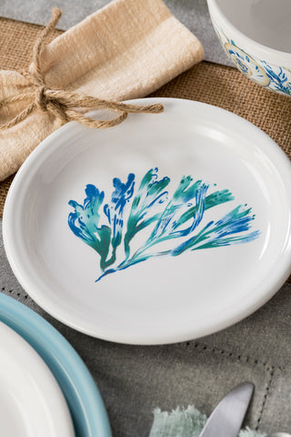 The Fiesta Retired Coastal Bistro Coupe 7 1/4 Inch Salad Plate, featuring a blue and green floral design, is made in the USA and displayed on a rustic table with a beige napkin, bowl, and fork.
