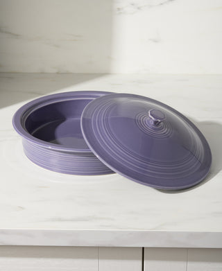 The Fiesta Lavender Small 10 Inch Round Covered Casserole, 1.4 Quart, with its matching lid slightly ajar, rests on a white marble countertop.