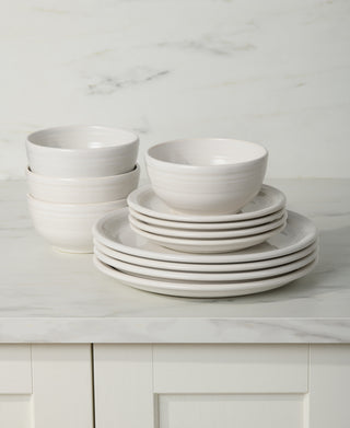 The Fiesta Bistro Coupe 12-Piece Dinnerware Set, Service for 4, features white bowls and plates neatly stacked on a light marble countertop in a kitchen with white cabinets and a marble backsplash.