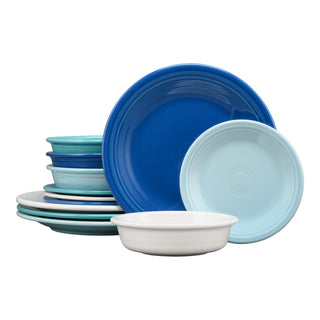 The Fiesta Mixed Coastal Blues Classic Rim 12-Piece Dinnerware Set, Service for 4, made in the USA, features ceramic plates and bowls in blue, light blue, teal, and white that overlap elegantly on a white background.