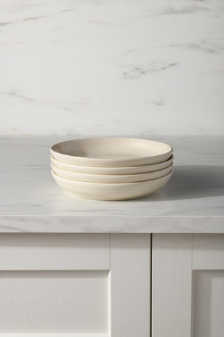 Four Fiesta Linen Coupe 8 1/2 Inch Luncheon Bowls, 26 OZ each, are stacked on a marble countertop in a kitchen with white paneled cabinets and a marble backsplash—perfect as a stylish white bowl set for serving meals. Set includes four bowls.