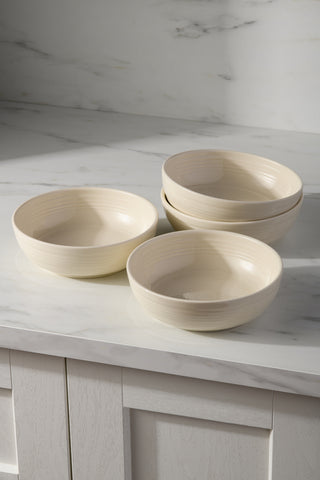 Four cream-colored Fiesta Linen Set of 4 Coupe 6 3/4 Inch Salad Bowls (24 OZ), made in the USA, are stacked on a white marble countertop with gray veining in a kitchen with light cabinets and a matching marble backsplash.