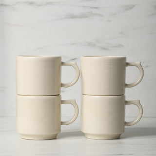 The Fiesta Linen 16 OZ Set of 4 Stackable Mugs, made in the USA and dishwasher safe, are cream-colored and shown stacked in two columns on a white countertop with a marble-patterned background.