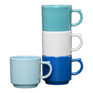 The Fiesta Coastal Blues 16 OZ Set of 4 Mixed Stackable Mugs includes a front coffee mug with three space-saving mugs in turquoise, white, and dark blue stacked behind it in a leaning tower.