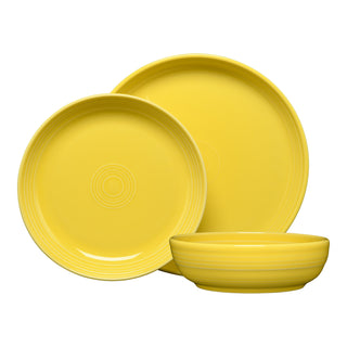 The Fiesta Coupe Bowl 3-Piece Place Setting features three yellow ceramic dishes—one coupe bowl and two round plates—standing upright with subtle rim patterns, creating a stylish, lead-safe china set.