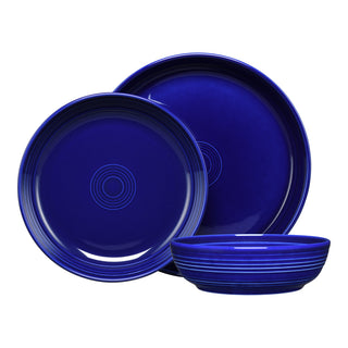 The Fiesta Coupe Bowl 3-Piece Place Setting features deep blue ceramic pieces: a plate, a larger plate behind, and a shallow bowl in front. Both plates have elegant concentric circle accents near the center.