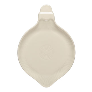 A cream-colored ceramic spoon rest with a rounded base, a small handle at the top, and concentric circular designs in the center.