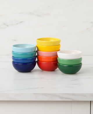 A stack of Fiesta 3 3/4 Inch Mini Bowl 5 OZ in blue, turquoise, yellow, red, green, and white by Fiesta is arranged on a white marble countertop with a light marble background.