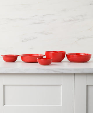 Five red ceramic bowls and plates, featuring the Fiesta 3 3/4 Inch Mini Bowl 5 OZ by Fiesta, are arranged in a row on a white marble countertop with a white cabinet and marble-patterned wall in the background.