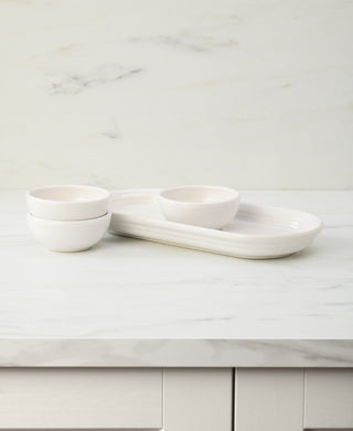 The Fiesta 4-Piece Condiment Set in White by Fiesta, featuring three small bowls and a matching tray, is arranged on a white marble countertop with a light marble backsplash in the background.