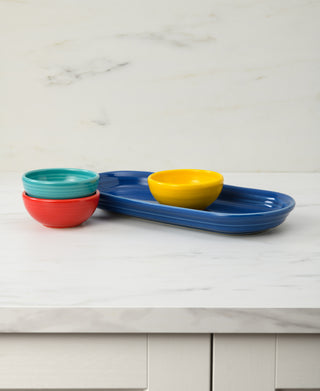 The Fiesta Vibrant Mixed Colors 4-Piece Condiment Set features four colorful mini bowls stacked beside and atop a long blue serving tray, adding a lively touch to your countertop.