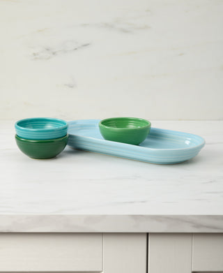 The Fiesta Aegean Mixed Colors 4-Piece Condiment Set features a light blue serving tray with three mini bowls in blue and green tones, displayed on a white marble countertop with a marble-patterned backsplash.