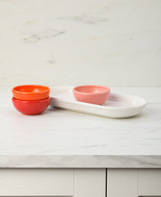 The Fiesta Sunset Horizon Mixed Colors 4-Piece Condiment Set features three vibrant mini bowls and a rectangular white tray, creating a cheerful accent on a marble countertop with a smooth, light background.
