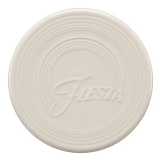 The Fiesta Extra Large Trivet 8 1/4 Inch in Linen is a round, off-white ceramic trivet with raised concentric circles and "Fiesta" embossed at the center, making it ideal as a heat-resistant table accessory.