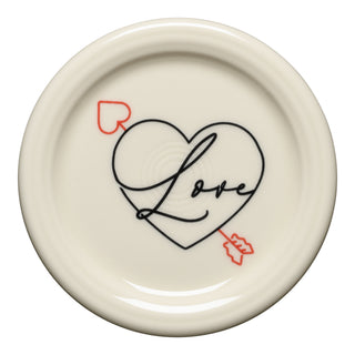 The Fiesta Valentine 4 3/8 Inch Coaster and Mug Cover is a round, cream piece with a black heart outline, "Love" in cursive, and a red arrow with a heart tail piercing the heart from lower left to upper right.