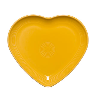 A daffodil yellow Retired Fiesta 9 Inch Heart Shaped Plate by Fiesta, featuring concentric circles in the center, is shown from above on a white background. Made in the USA.