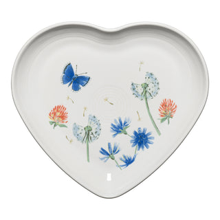 The Fiesta Retired Breezy Floral 9 Inch Heart Shaped Plate features blue butterflies, wildflowers, and dandelions on white china. This lead-safe plate is dishwasher safe and made in the USA.