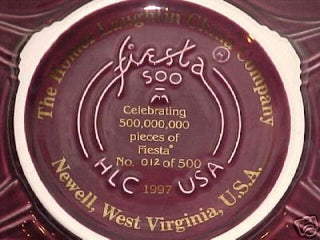 A maroon ceramic plate with gold text reads: The Homer Laughlin China Company, Fiesta, Celebrating 500,000,000 pieces of Fiesta, No. 012 of 500, HLC USA, 1997, Newell, West Virginia, U.S.A.