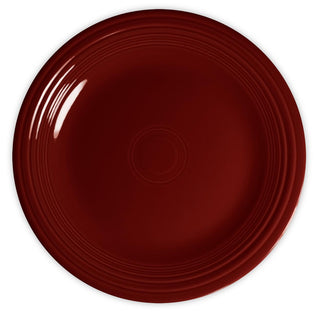 A round, dark red ceramic plate with a glossy finish and concentric circular ridges along the rim, viewed from above on a white background.