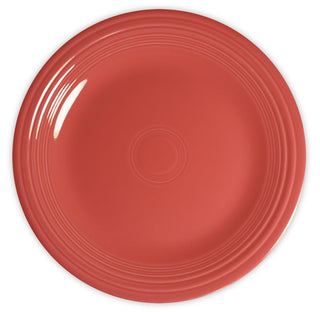 A round, coral-red ceramic plate viewed from above, featuring concentric circular ridges along the rim and a glossy finish.