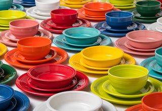A variety of colorful ceramic dishware sets, including bowls, plates, and saucers, are neatly arranged in rows. Each set features matching pieces in vibrant colors like red, yellow, blue, green, orange, and white.