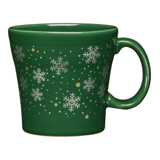 The Fiesta Snowflake 15 OZ Tapered Mug is a green ceramic mug made in the USA, featuring white snowflakes and gold dots. It is microwave safe and photographed on a white background.