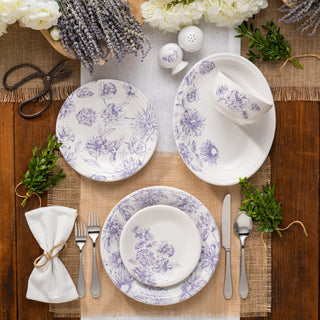 Set table with floral-patterned plates, silverware, and decorative elements on a wooden surface.